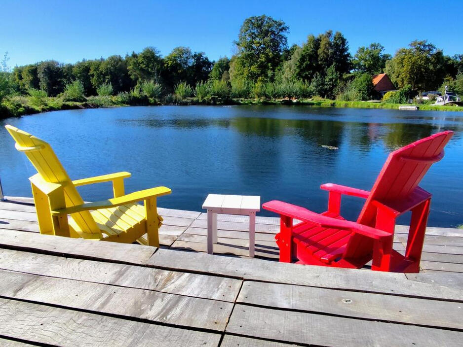 Entspannung am Mühlenteich Bunte Adirondack-Stühle auf einem Holzsteg direkt am Mühlenteich der Wassermühle Bruchmühlen – ein idyllischer Ort zum Entspannen und Genießen der Natur.