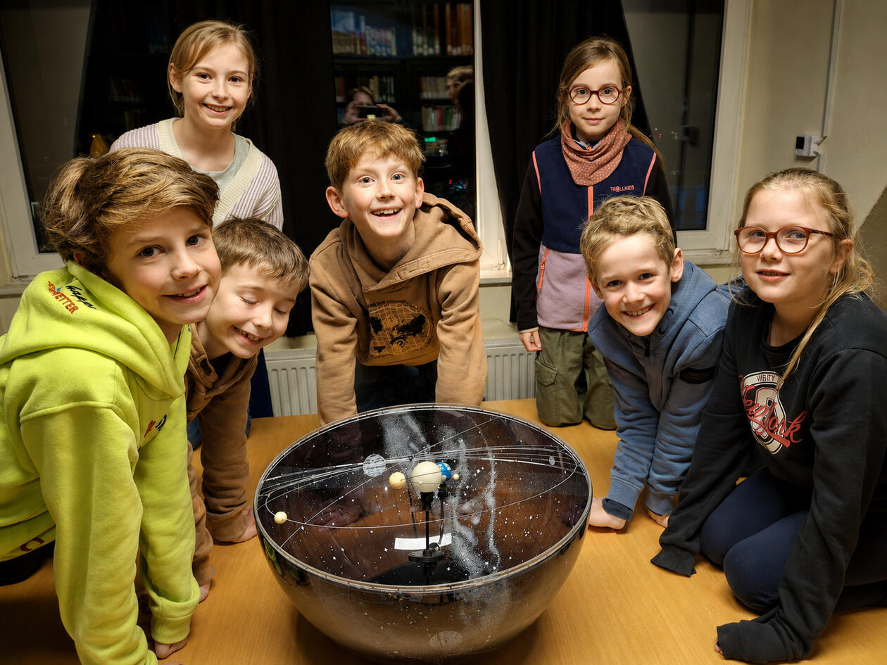 Kinder entdecken das Planetarium Mehrere Kinder stehen begeistert um ein Planetarium und beobachten die Bewegung der Planeten während einer spannenden Astronomie-Vorführung.